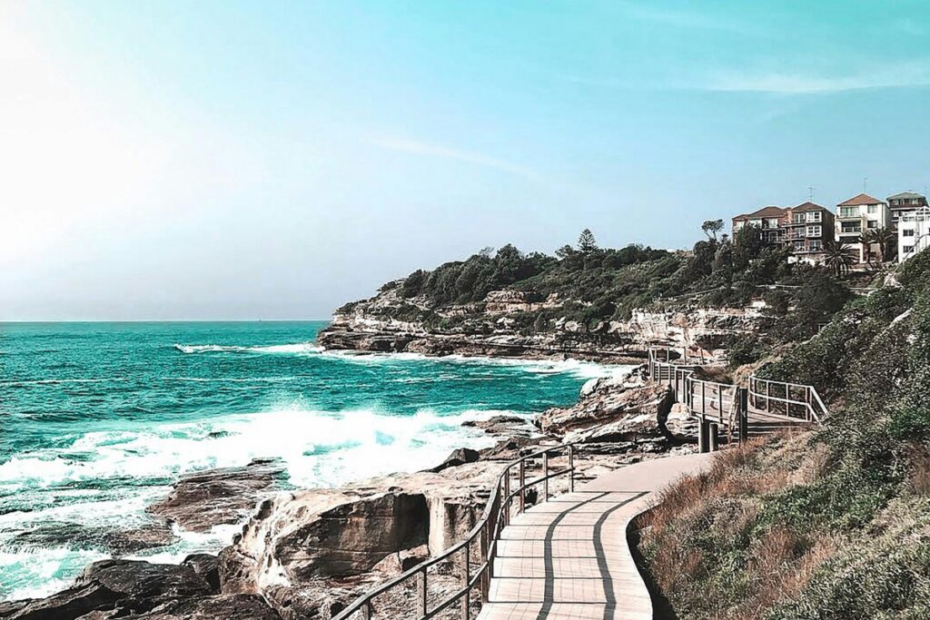 A scenic coastal path in Australia winds along rocky cliffs, with the turquoise ocean waves crashing below and houses perched on the hilltop. Just as this path offers a unique journey along the shore, "Twitter en Australia: estrategias para influencers. Aprende a crear tweets cautivadores, usar herramientas de Twitter y monetizar. Conoce tendencias como Twitter Spaces y Twitter Blue" guides influencers on a path to success on the Twitter platform in Australia.