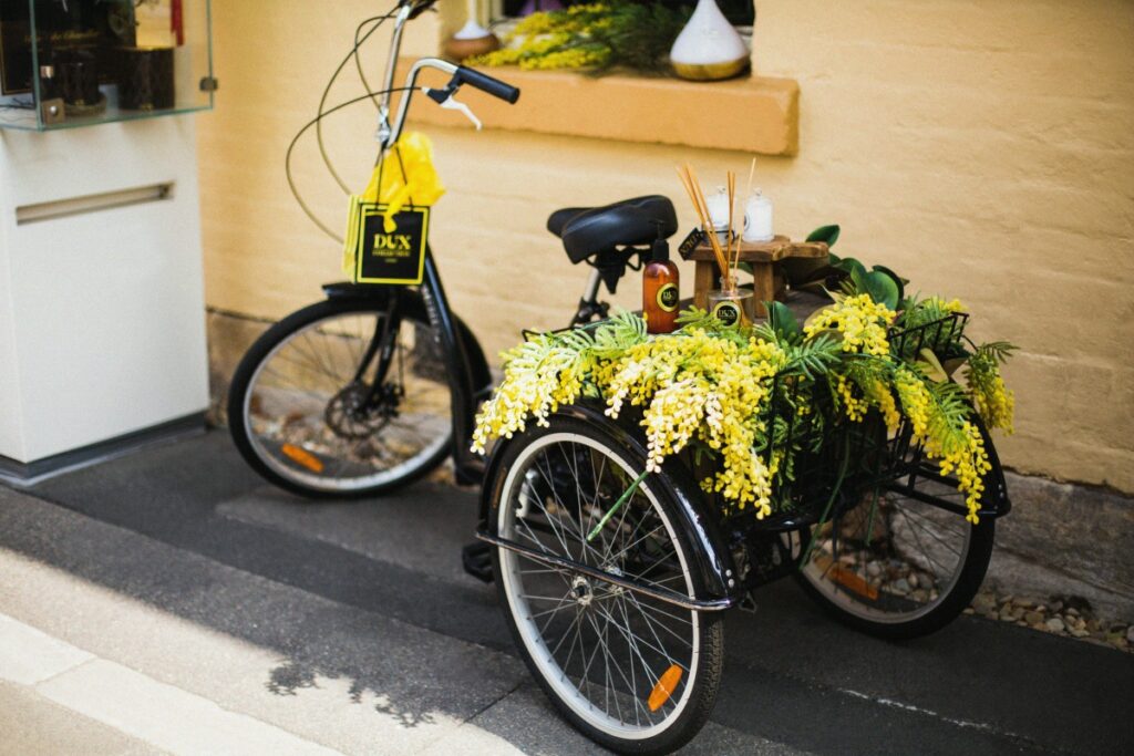 A charming tricycle, adorned with vibrant yellow wattle flowers and some products, is parked beside a building. Just as this tricycle can be a unique way to showcase items, "WhatsApp for Business in Australia: A Full Guide" offers a comprehensive way for Australian businesses to connect with customers and showcase their services on the WhatsApp platform.